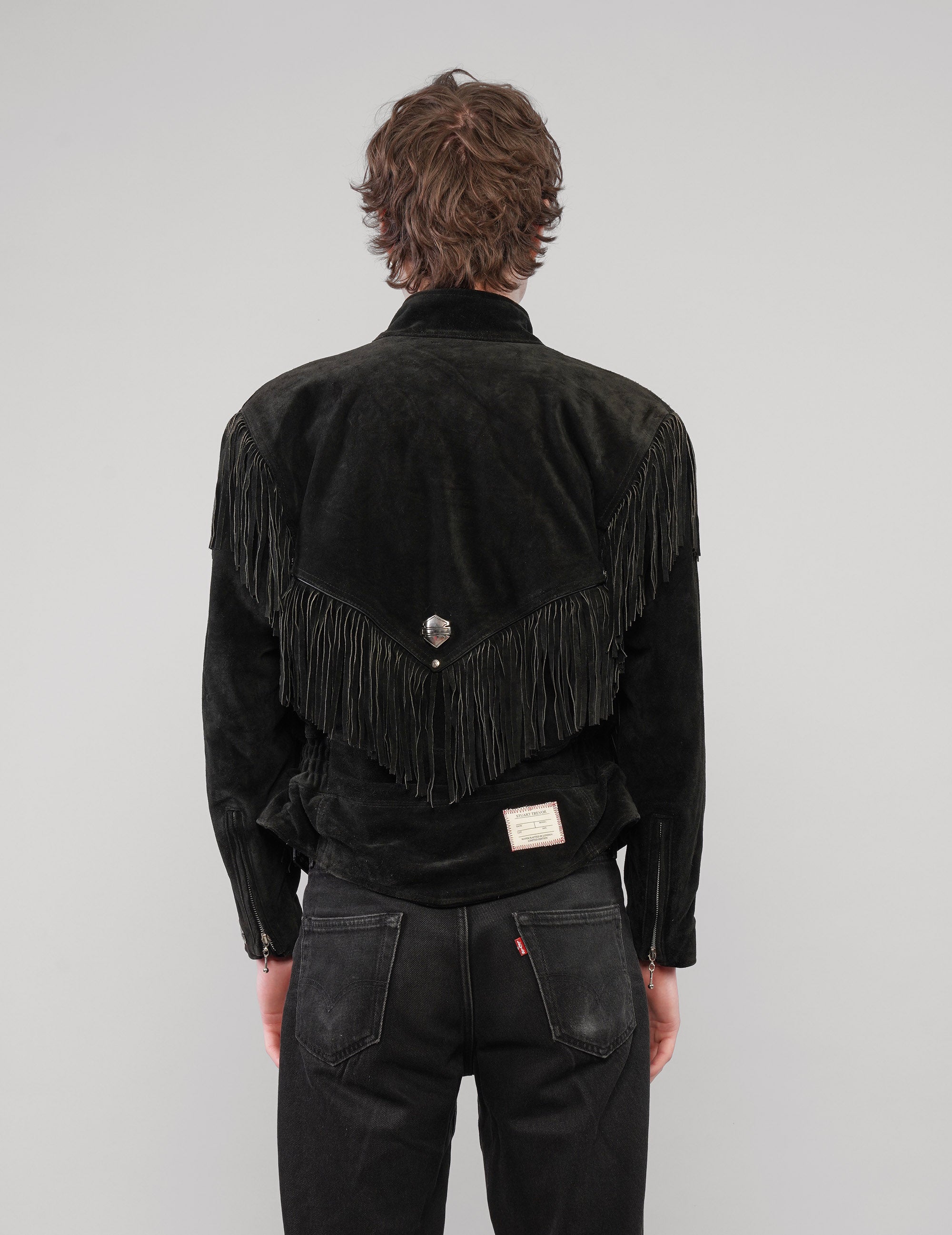 Back view of the black jacket showing the pointed fringed yoke and metal badge.
