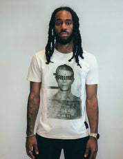 A person wearing an ecru-colored t-shirt with a large cool photo x and 
inferno mask graphic and the text 'Saint' on it.
