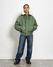 Green N-2B flying jacket worn zipped, showing the fur-trimmed hood and storm flap