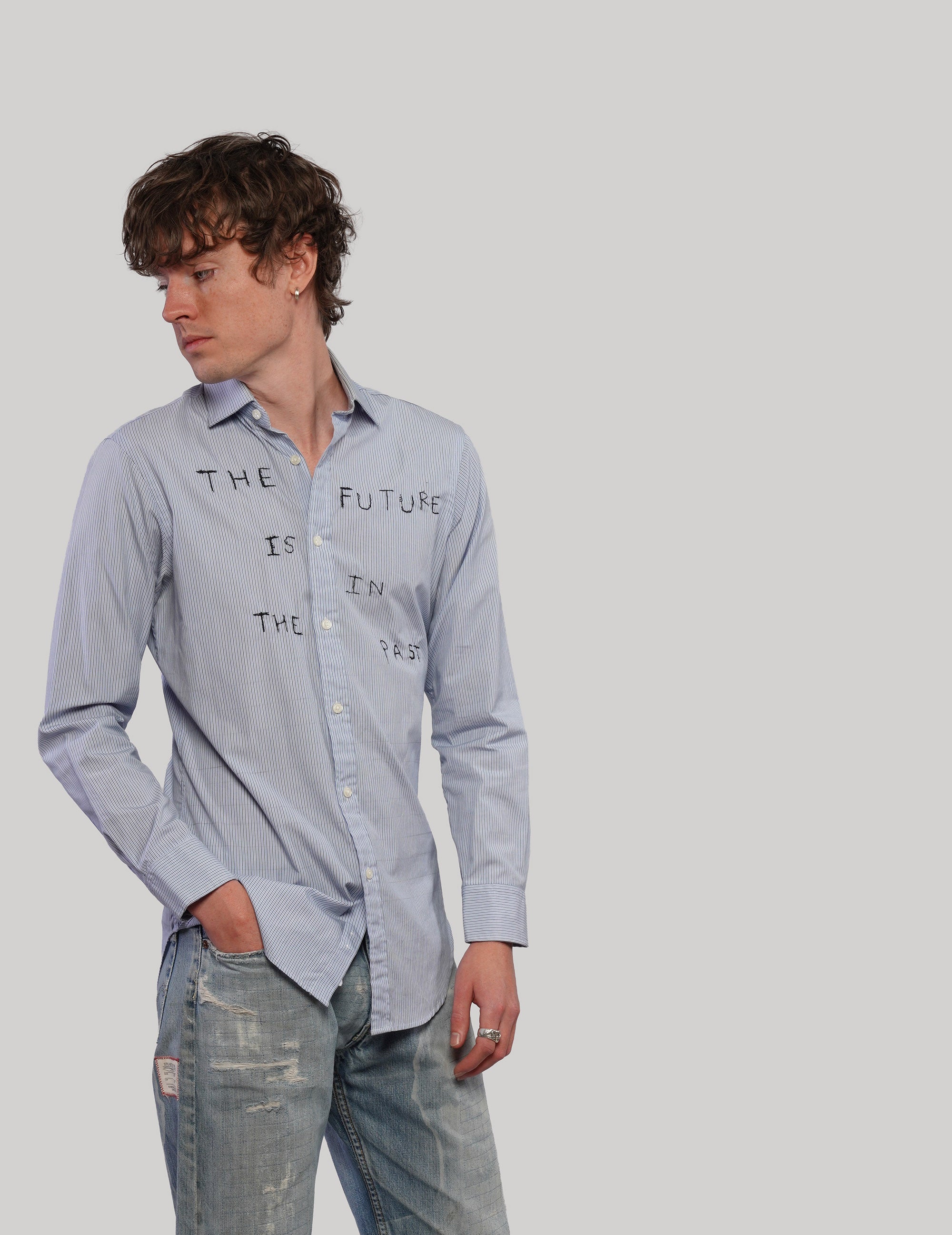 Angled front view of a light blue pinstripe graphic shirt with pointed collar, styled with blue jeans.