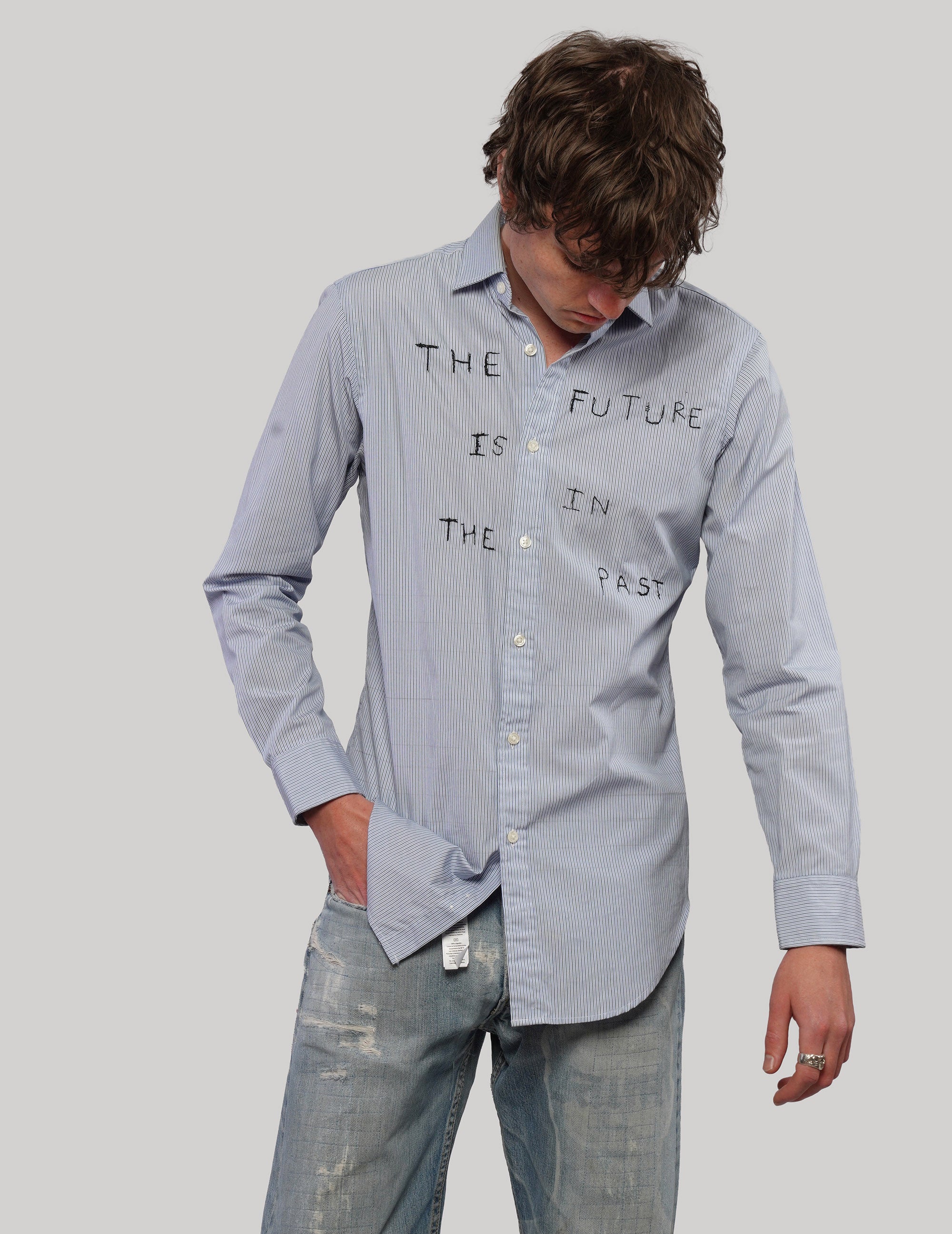 Model looking down while wearing a light blue pinstripe Future Is in the Past shirt with long sleeves.