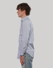 Side profile of model wearing a light blue pinstripe long-sleeve shirt with curved hem.
