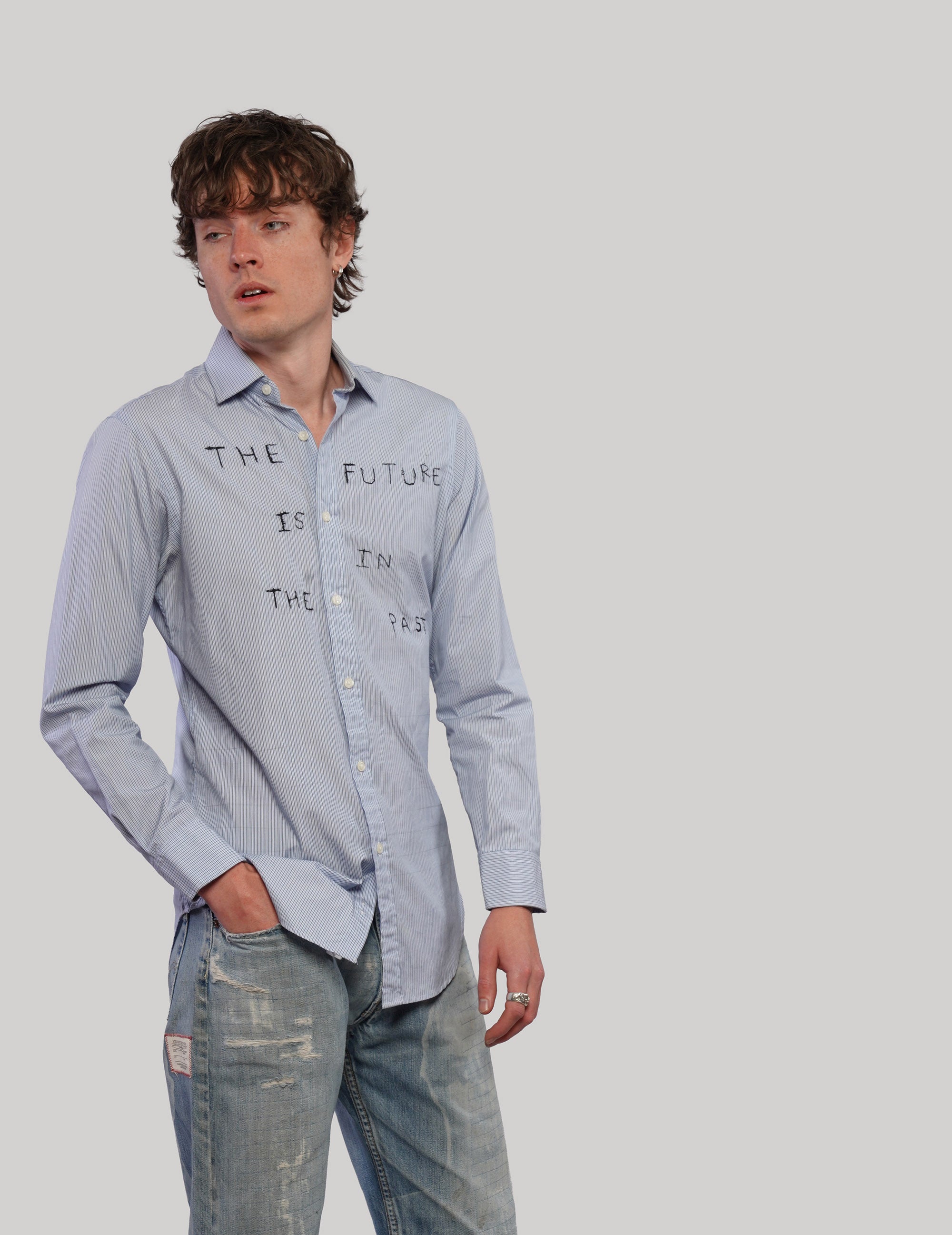 Model wearing a light blue Future Is in the Past shirt with black graphic lettering, styled with distressed jeans.