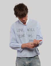 Model looking down while adjusting the sleeve of a light blue pinstripe Love Will cropped shirt.