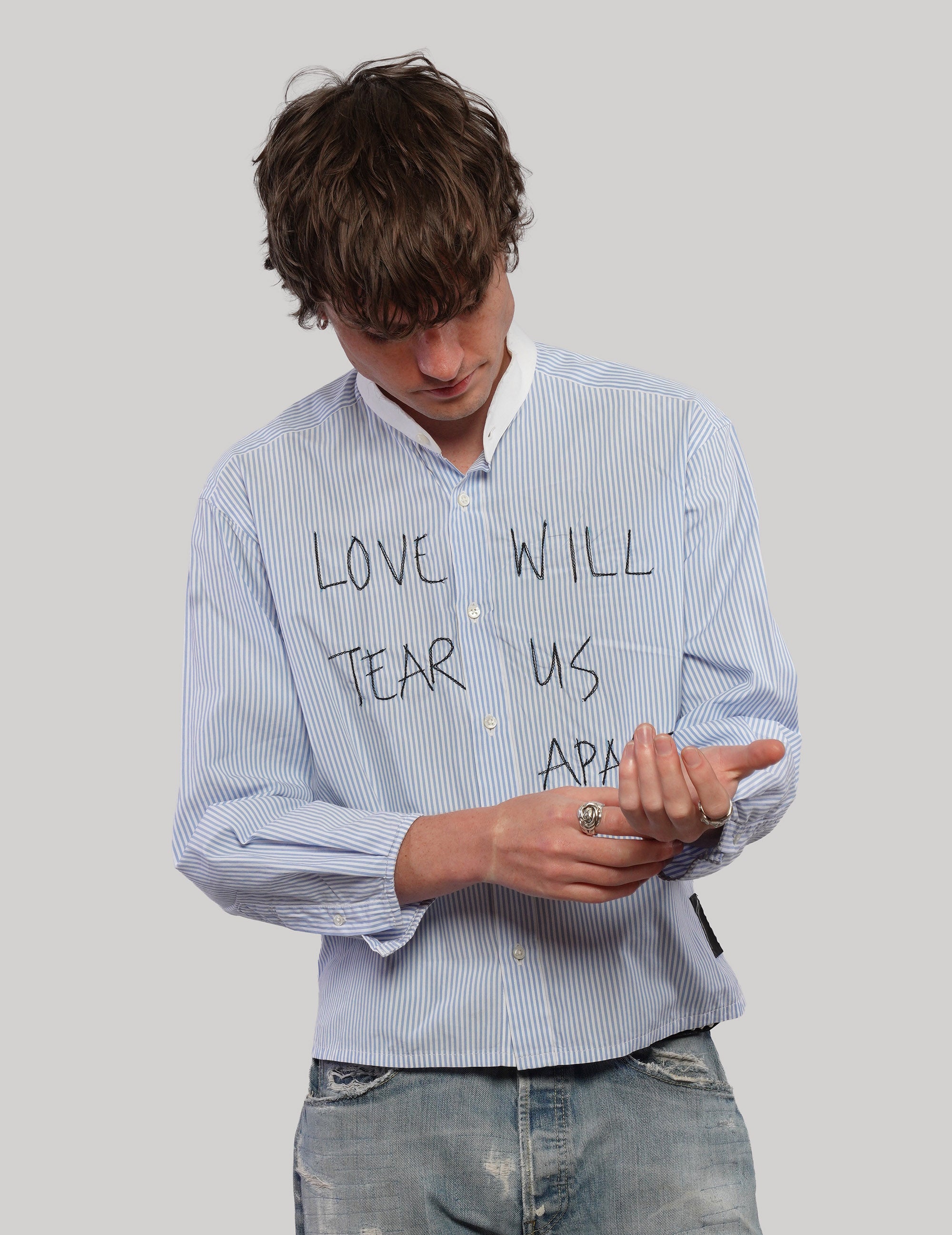Model looking down while adjusting the sleeve of a light blue pinstripe Love Will cropped shirt.