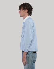 Side view of a light blue pinstripe Love Will cropped shirt with long sleeves, white collar and straight hem.