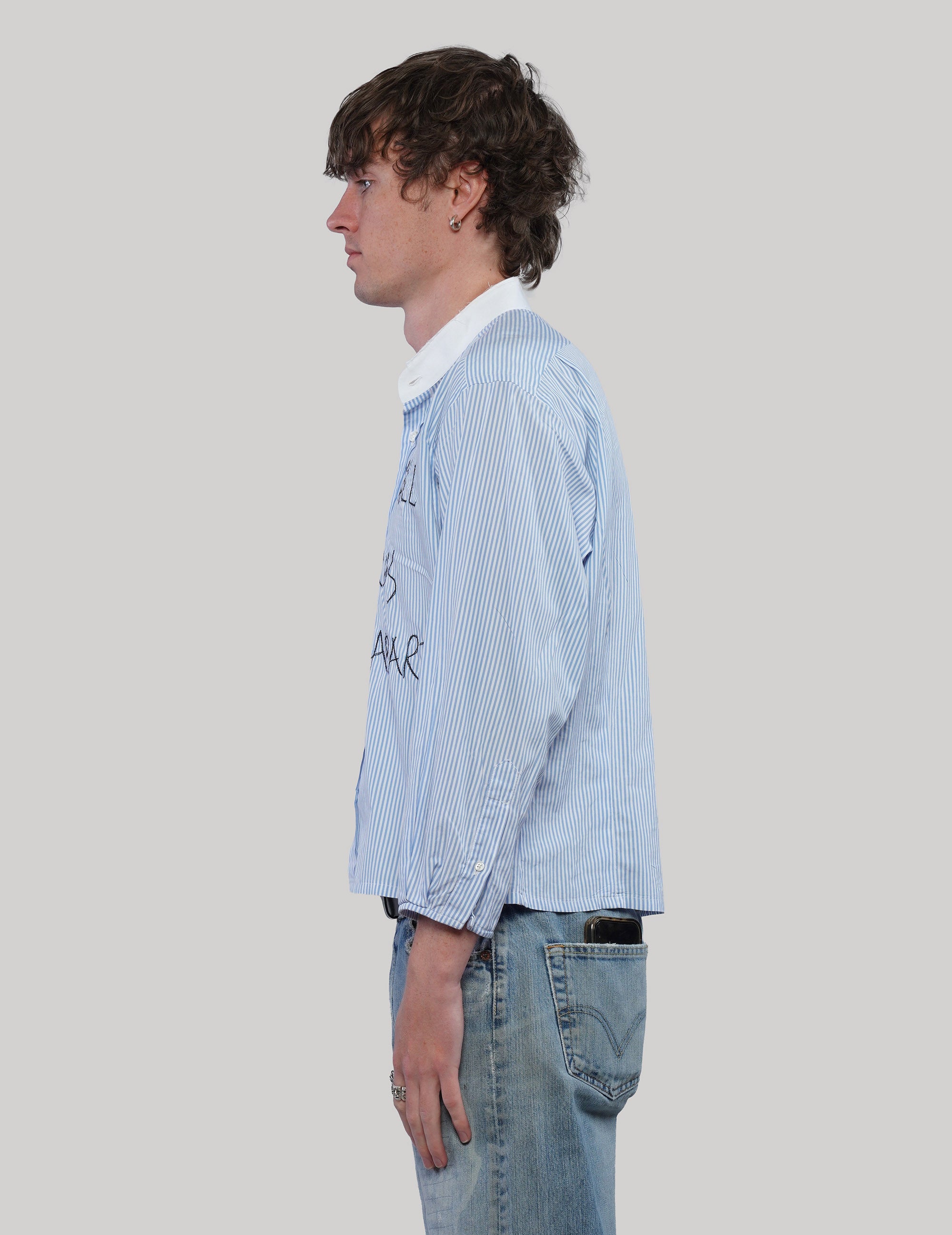 Side view of a light blue pinstripe Love Will cropped shirt with long sleeves, white collar and straight hem.