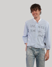 Smiling model wearing a light blue pinstripe Love Will cropped shirt with black lettering, styled with distressed blue jeans.
