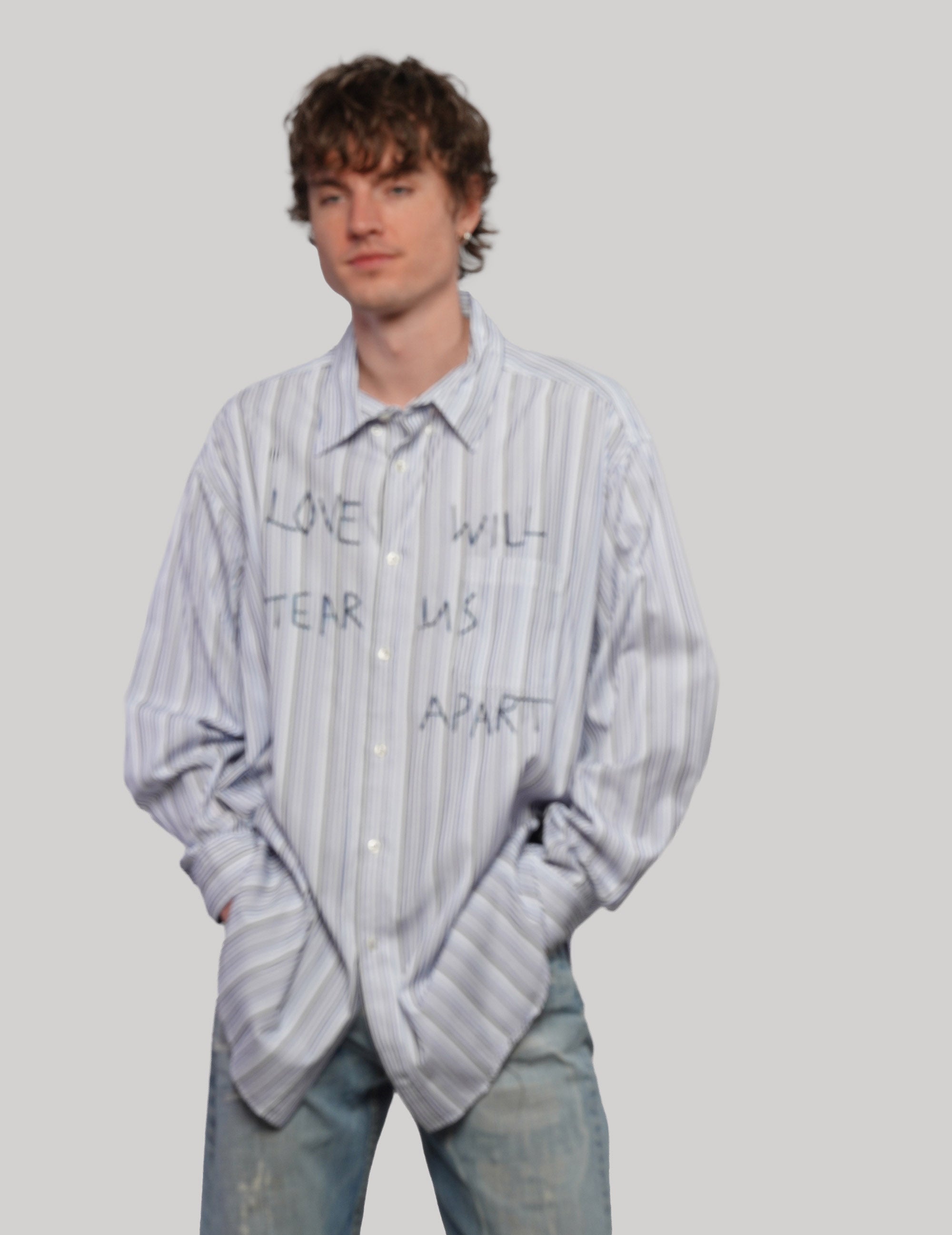Model wearing a blue and white multi-stripe Love Will shirt with black graphic lettering and a relaxed silhouette.