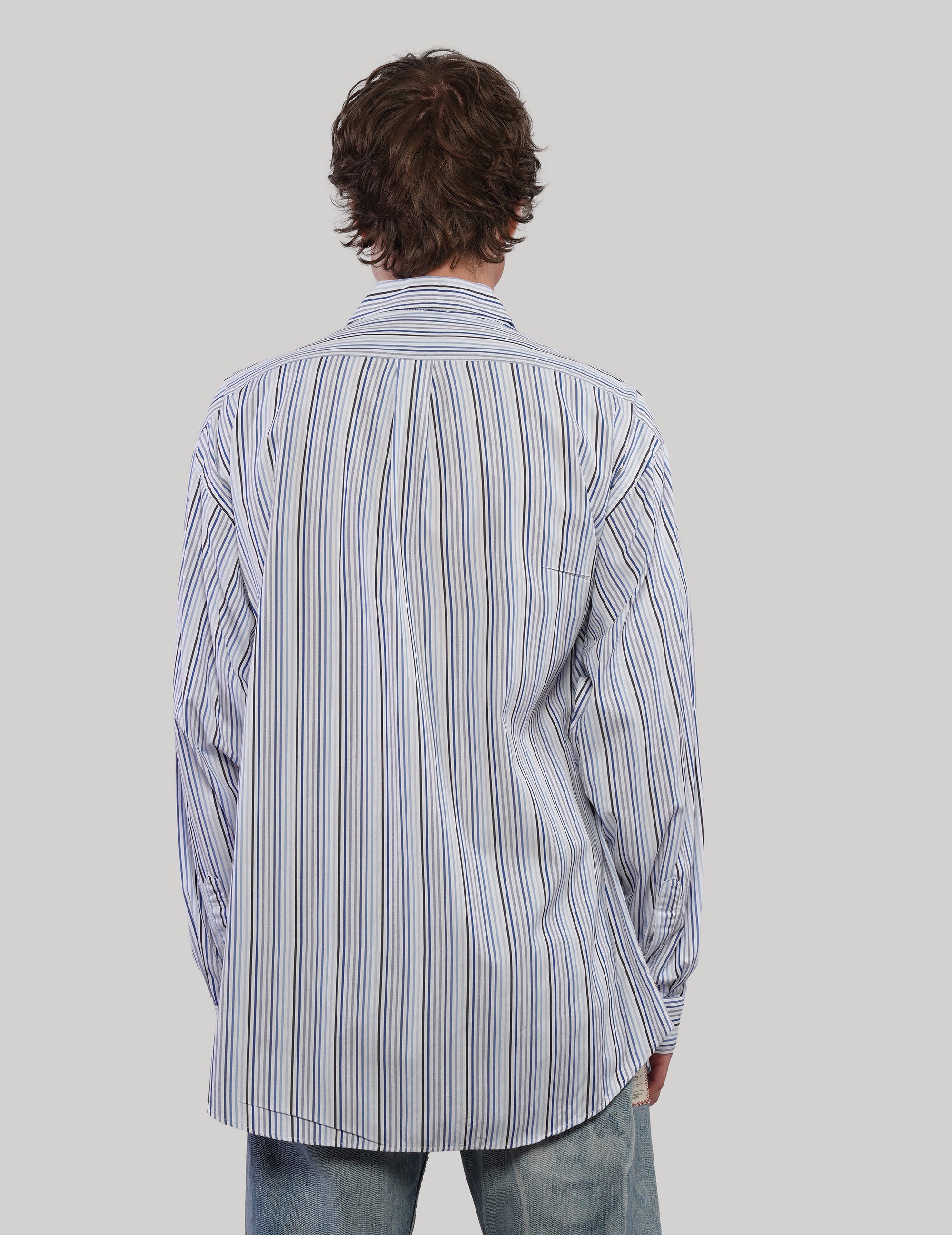Back view of a blue multi-stripe cotton shirt showing vertical stripes of varying widths and long cuffed sleeves.