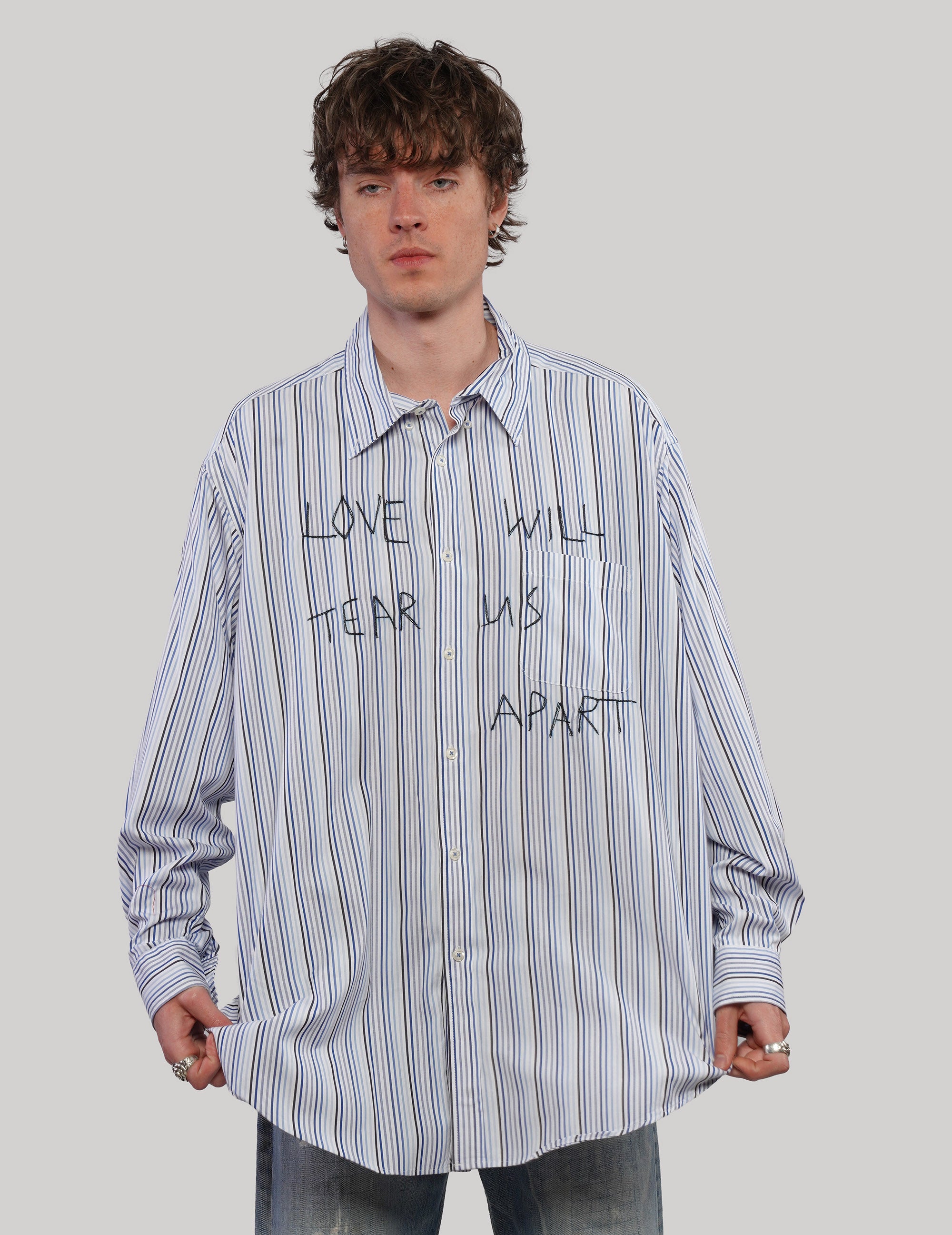Front view of model wearing a blue Love Will striped shirt with black lettering, pointed collar and long sleeves.