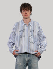 Model wearing an oversized blue striped Love Will cotton shirt with the front partially tucked into faded jeans.