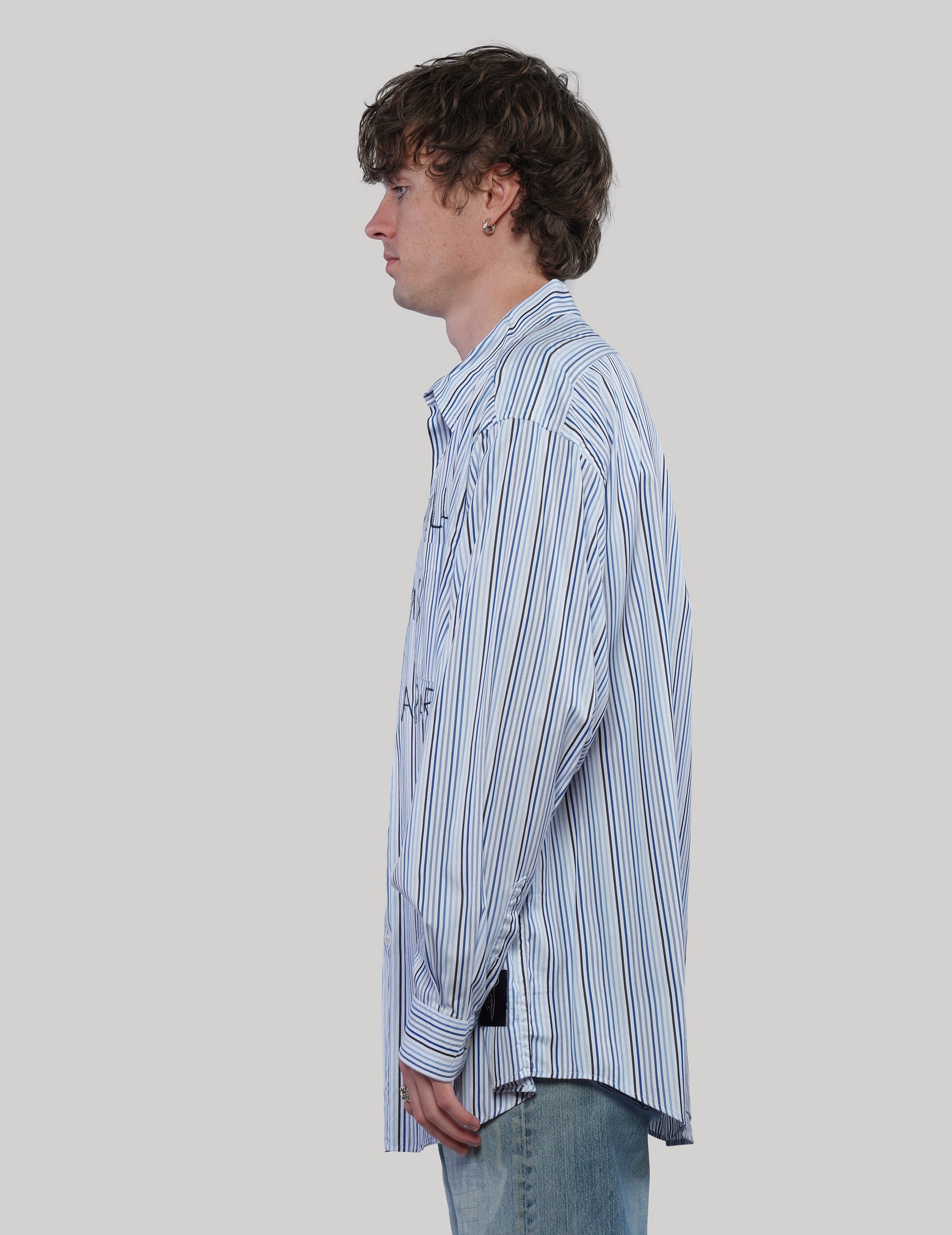 Side profile of model wearing a blue multi-stripe Love Will shirt with long sleeves and a curved hem.