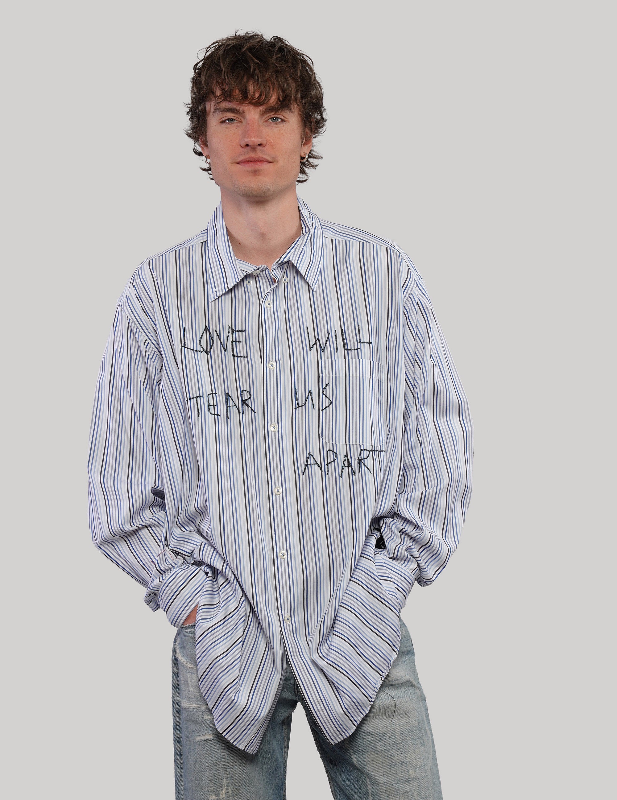 Model wearing a loose-fitting blue Love Will multi-stripe shirt with hands in pockets, styled with light blue jeans.