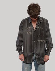 Model looking down wearing a black and white pinstripe shirt with light 'Love Will' lettering across the front.
