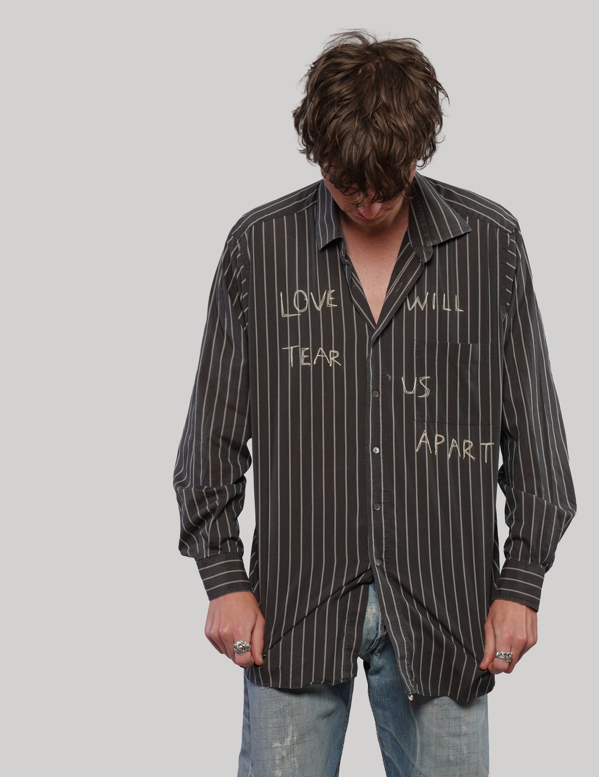 Model looking down wearing a black and white pinstripe shirt with light 'Love Will' lettering across the front.