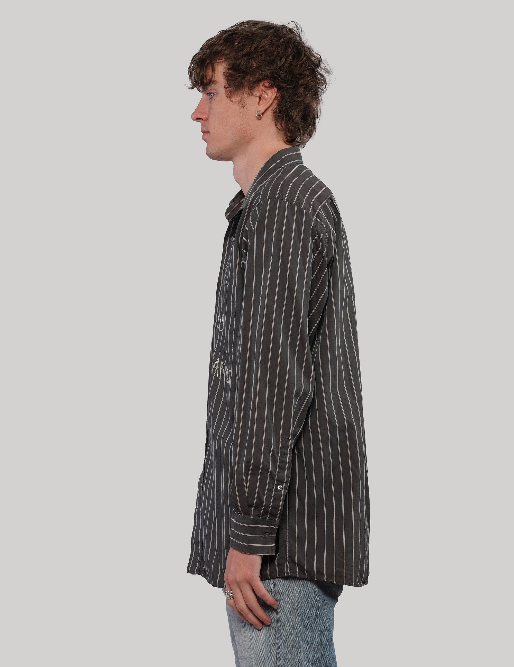 Side profile of a black pinstripe cotton shirt showing its pointed collar, long sleeves and relaxed silhouette.