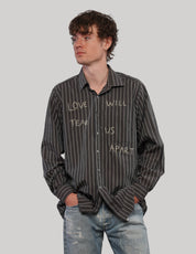 Model wearing a black 'Love Will' pinstripe shirt with hands in jeans pockets, showing the front graphic lettering.