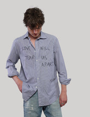 Model looking down wearing a blue striped 'Love Will' shirt with black front lettering, rolled sleeves and distressed jeans.