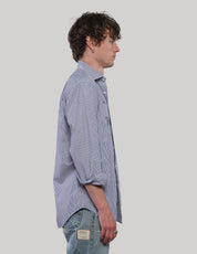 Side view of a blue and white vertically striped cotton shirt showing its loose silhouette, long sleeves and curved hem.