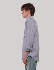 Side profile of model wearing a blue pinstripe 'Love Will' shirt with pointed collar, rolled sleeves and a curved hem.