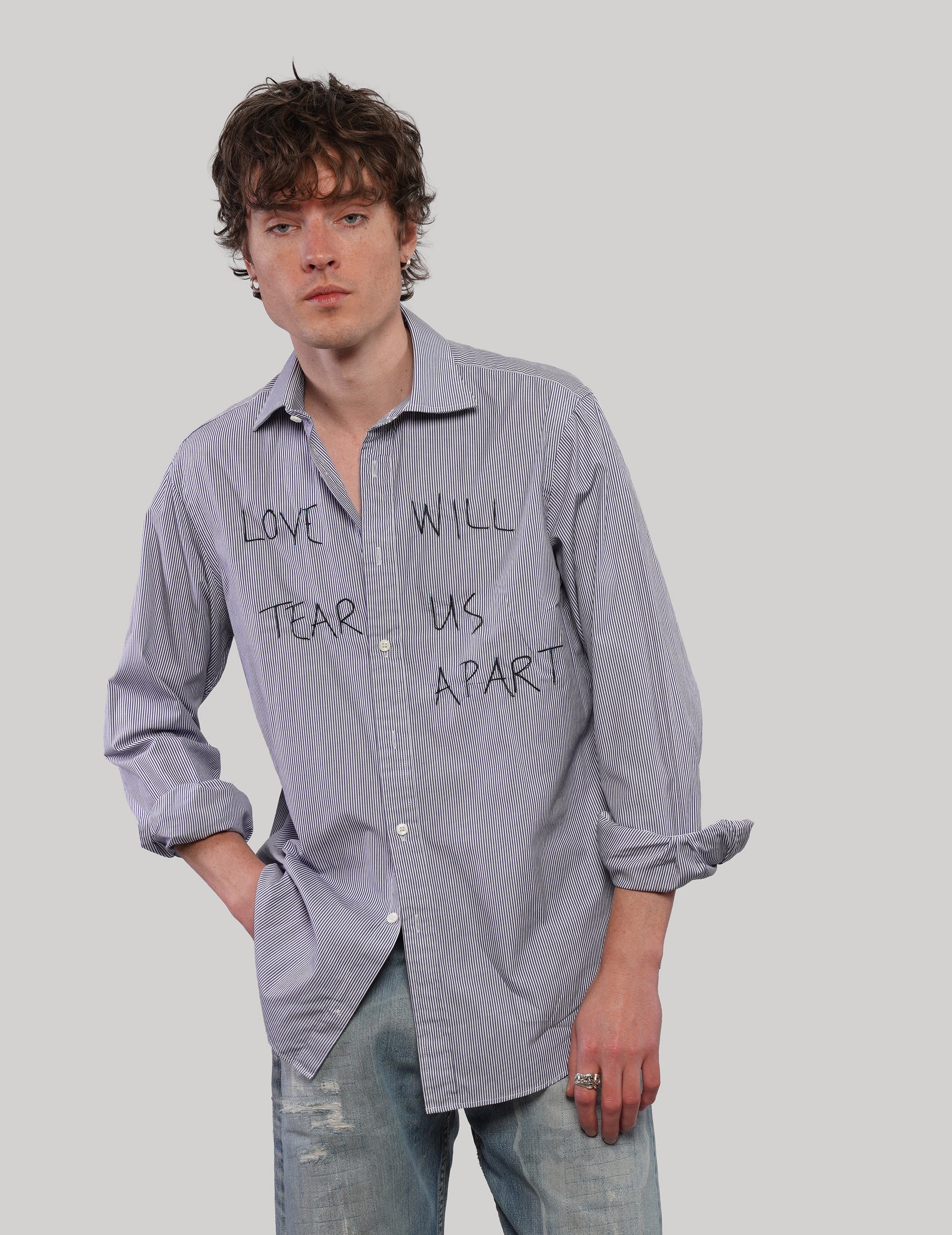 Model wearing an upcycled blue T.M.Lewin pinstripe shirt with black 'Love Will' graphic lettering, styled with faded blue jeans.
