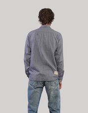 Back view of a grey upcycled vintage shirt showing long sleeves, a relaxed fit and curved hem, styled with blue jeans.