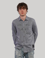 Model wearing a grey 'Love Will' cotton shirt with black handwritten-style lettering, pointed collar and dark buttons.