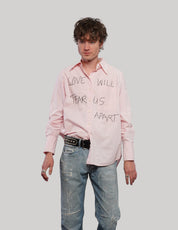 Model wearing a pink upcycled COS shirt with black 'Love Will' graphic lettering and long cuffed sleeves.
