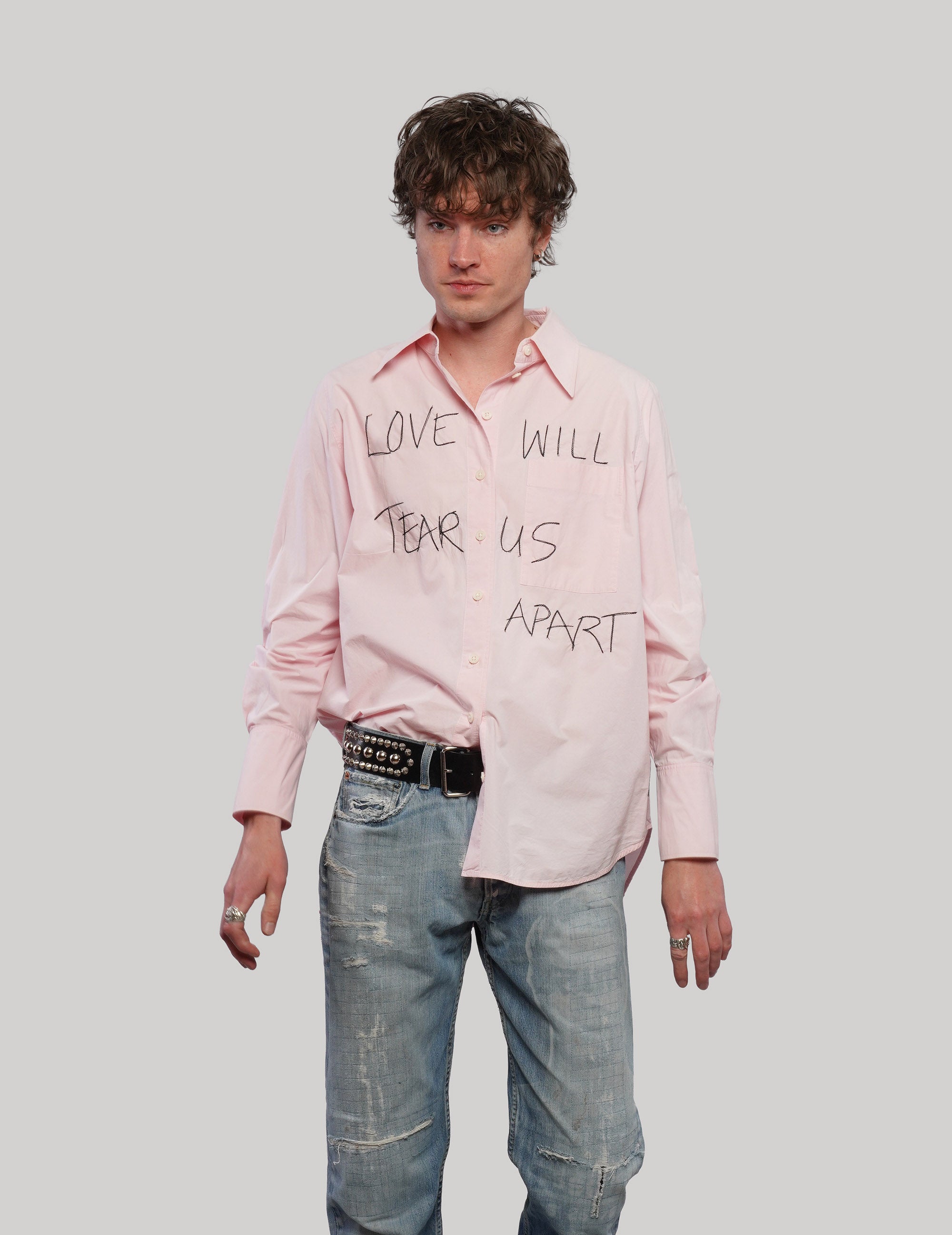 Model wearing a pink upcycled COS shirt with black 'Love Will' graphic lettering and long cuffed sleeves.