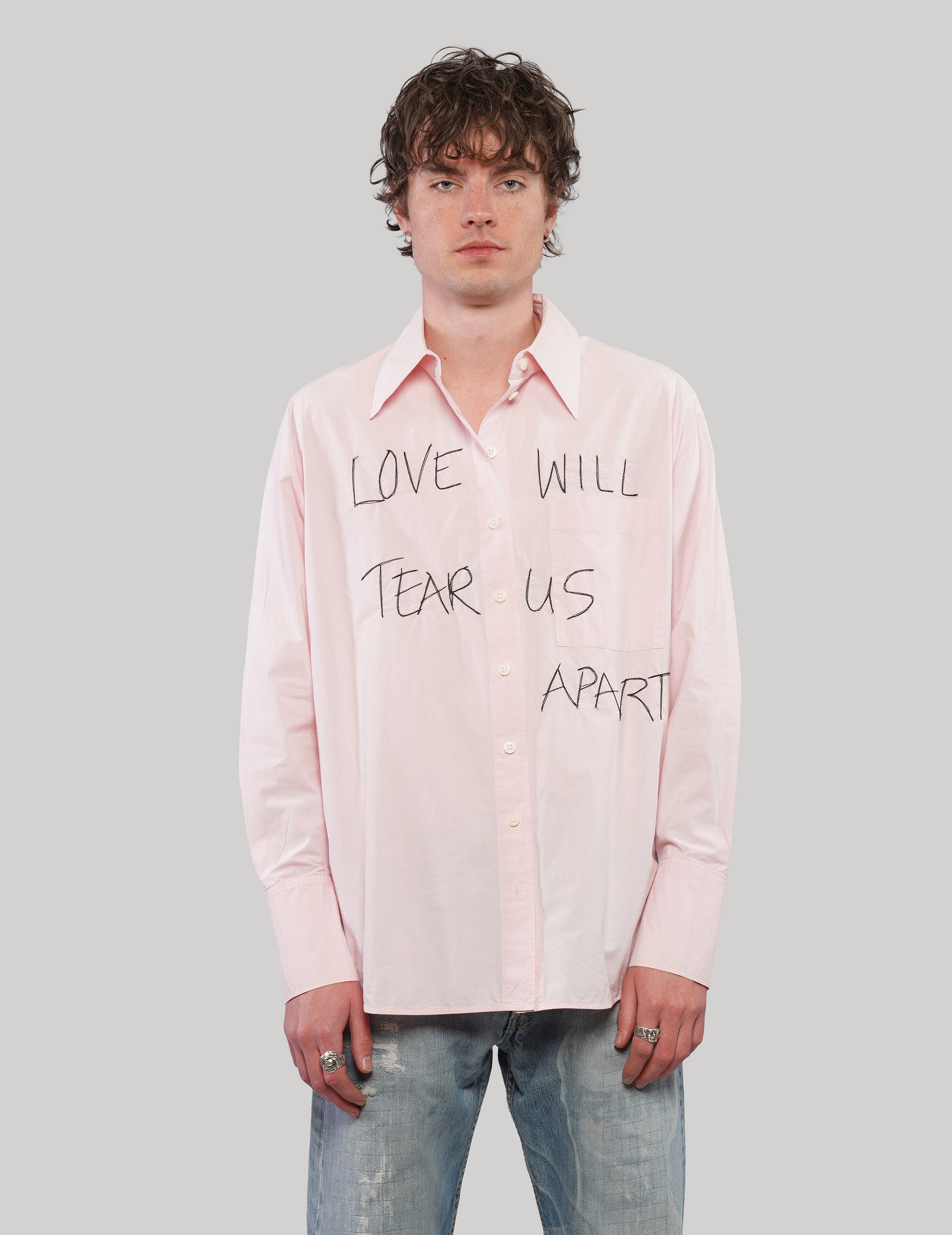 Front view of a pink 'Love Will' cotton shirt with black handwritten-style lettering, pointed collar and button fastening.