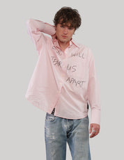 Model wearing a pink 'Love Will' cotton shirt with black graphic lettering, one hand resting behind his head.