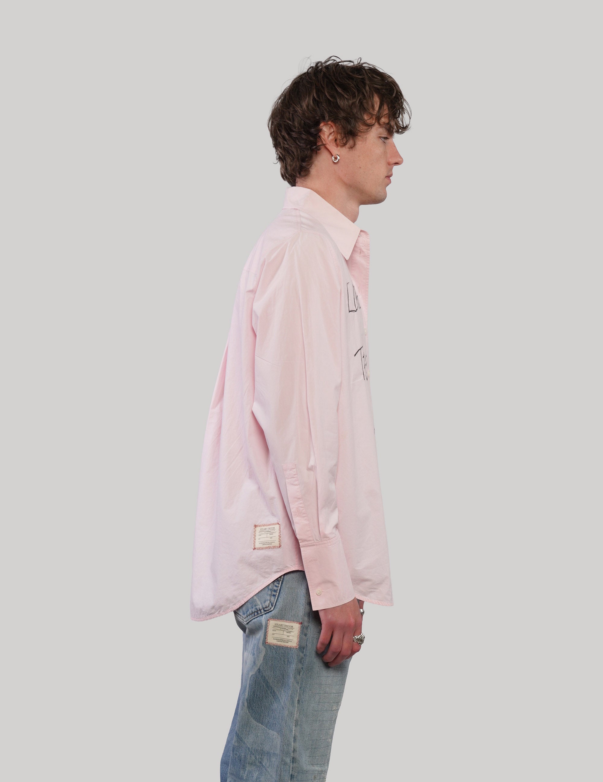 Side profile of model wearing a pink COS cotton shirt with long sleeves, button cuffs and a curved hem.