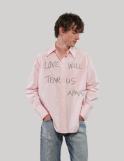 Model wearing a pink 'Love Will' cotton shirt with black front lettering, one hand in his jeans pocket.