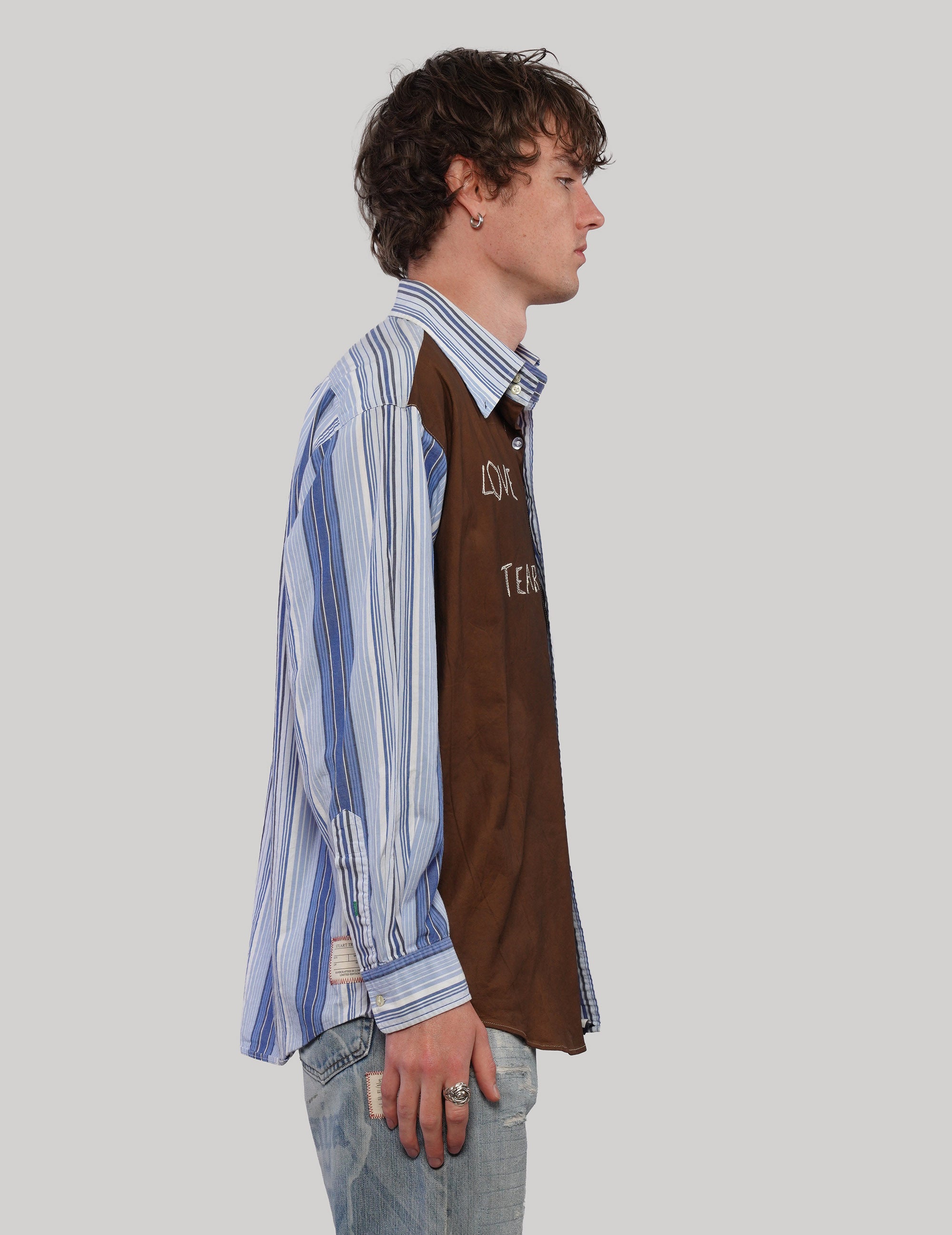 Side profile showing the brown front panel of the 'Love Will' split shirt against blue and white striped sleeves.
