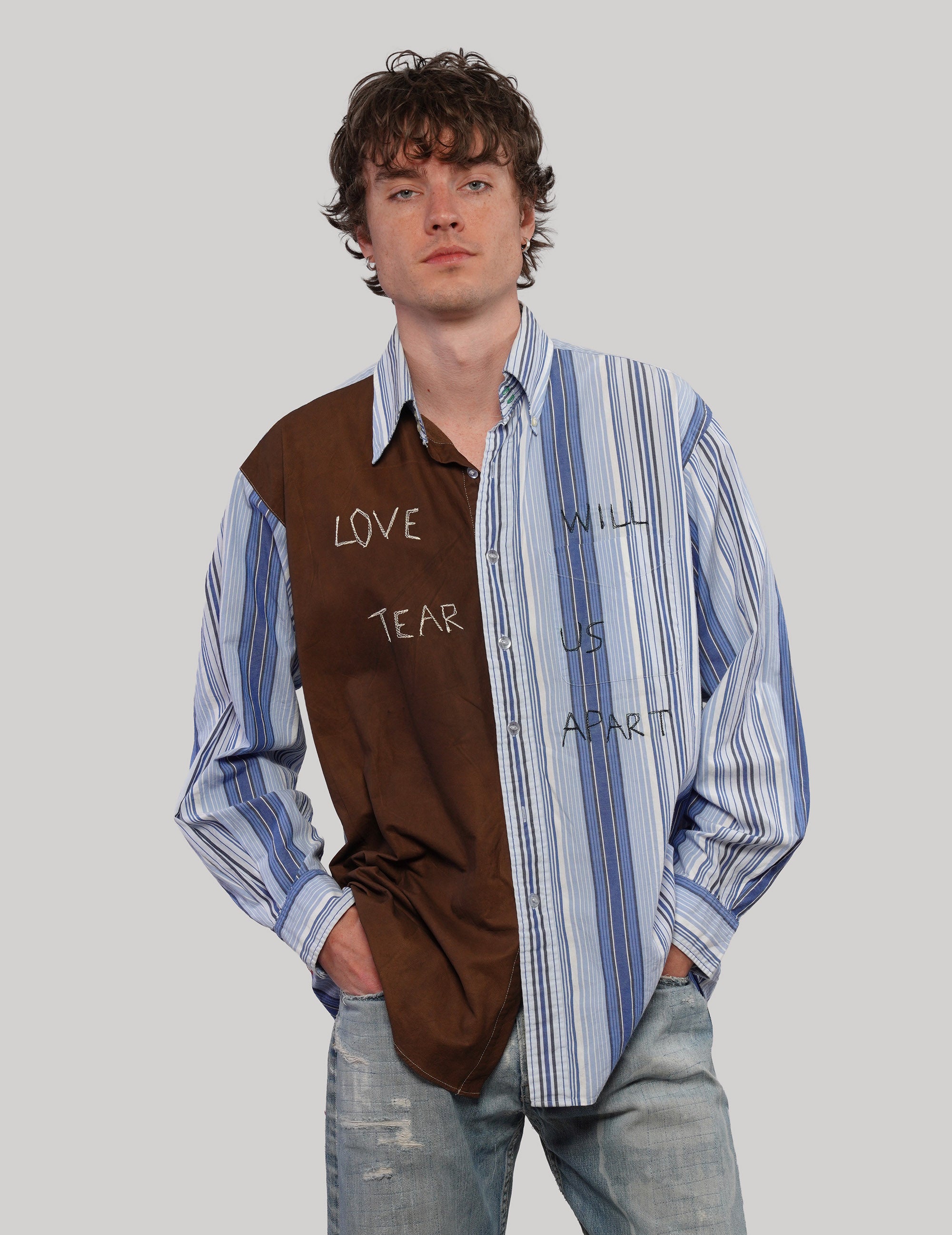 Model wearing a brown and blue 'Love Will' split shirt with contrasting striped panels and handwritten graphic lettering.