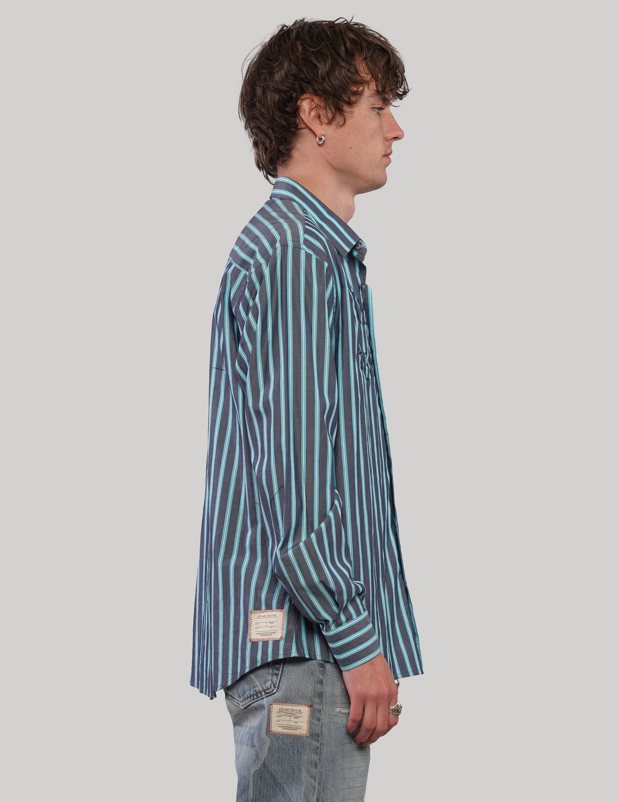 Side view of a teal and light blue vertically striped shirt showing the pointed collar, long sleeves and loose silhouette.