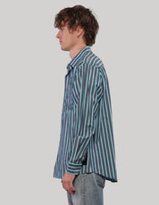 Side profile of model wearing a teal striped 'Love Will' cotton shirt with a relaxed fit and curved hem.