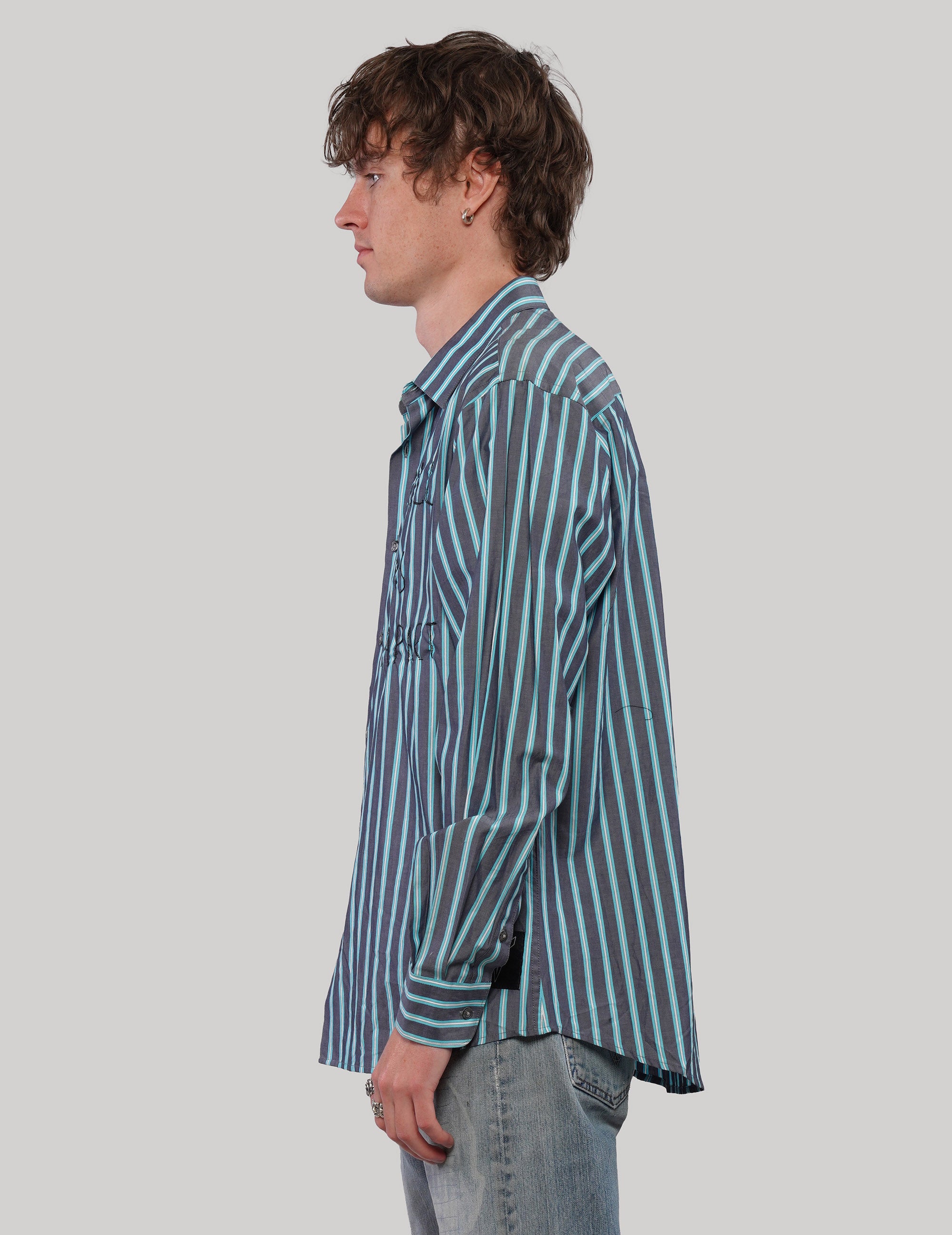 Side profile of model wearing a teal striped 'Love Will' cotton shirt with a relaxed fit and curved hem.