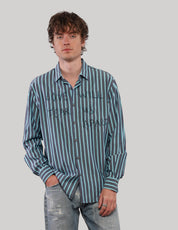 Model wearing a teal striped 'Love Will' cotton shirt with hands in pockets, styled with distressed blue jeans.