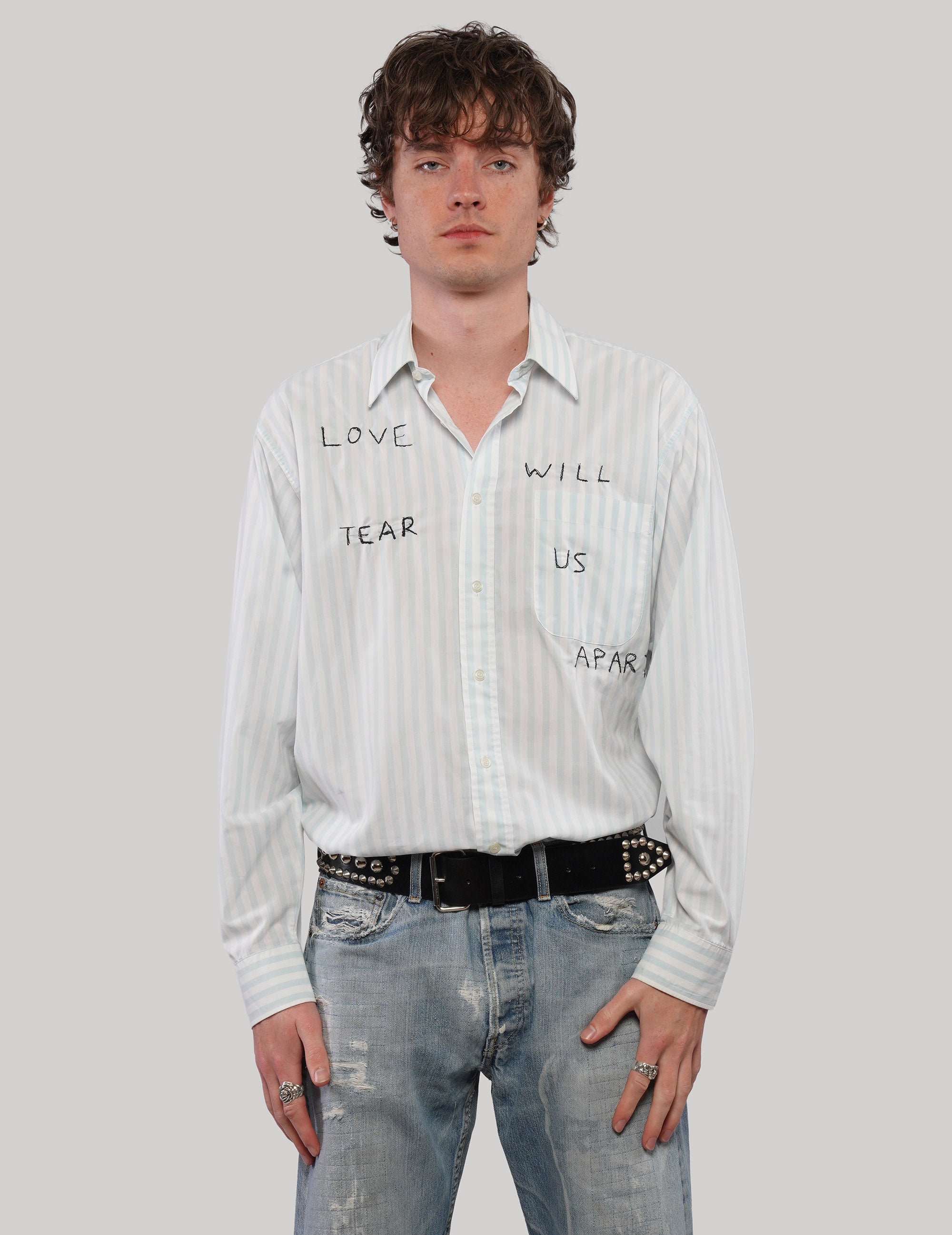 Model wearing a white 'Love Will' striped shirt with pale green and yellow lines and black graphic lettering.