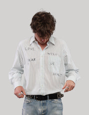 Model looking down while adjusting a white striped 'Love Will' shirt with long sleeves and graphic lettering.