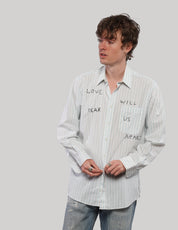 Model wearing a white striped 'Love Will' cotton shirt with pointed collar and black lettering, styled with jeans.