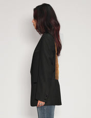 Side view of model wearing a black vintage tuxedo jacket with gold sequin back panel, styled with blue jeans.