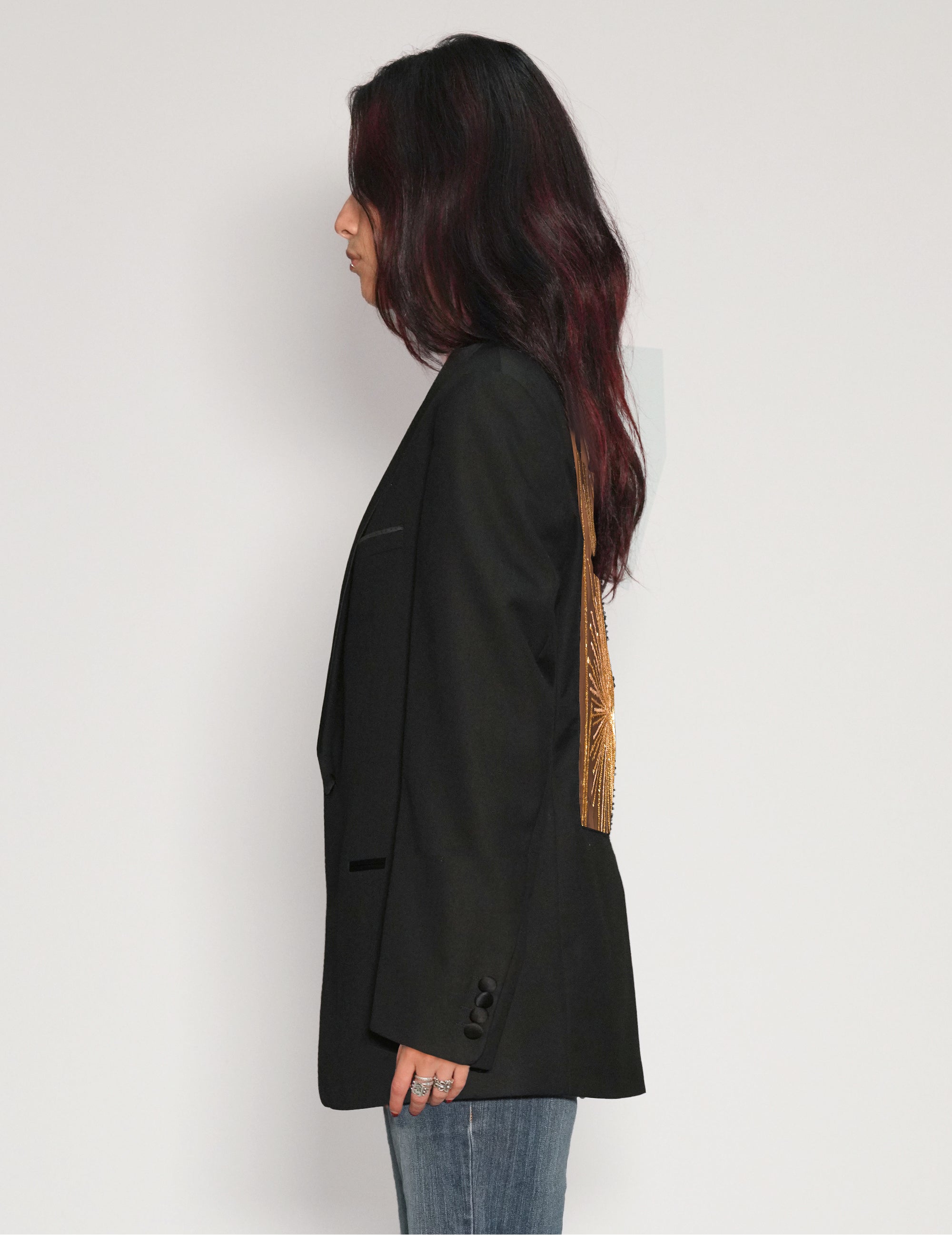 Side view of model wearing a black vintage tuxedo jacket with gold sequin back panel, styled with blue jeans.