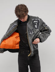 Model holding the charcoal patched bomber jacket open to reveal its bright orange lining and front graphic patches.