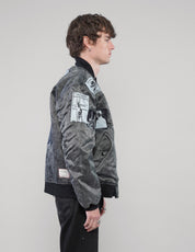 Right-side view of a model wearing the charcoal bomber jacket, showing graphic sleeve patches and ribbed cuffs.