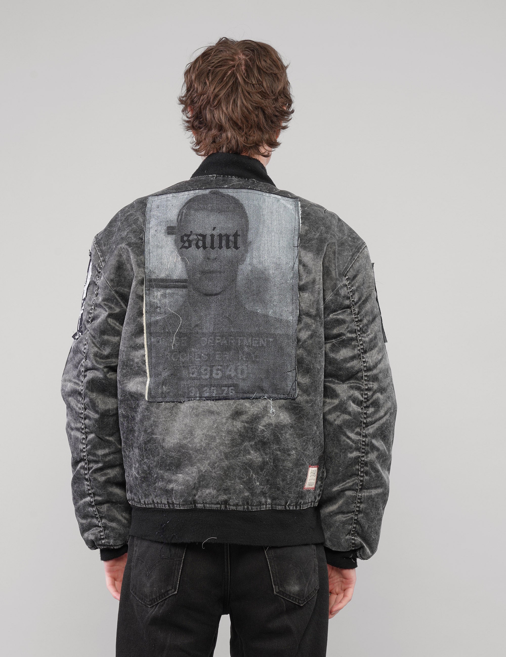 Back view of the charcoal patched bomber jacket on a model, showing the large rectangular Saint graphic patch.