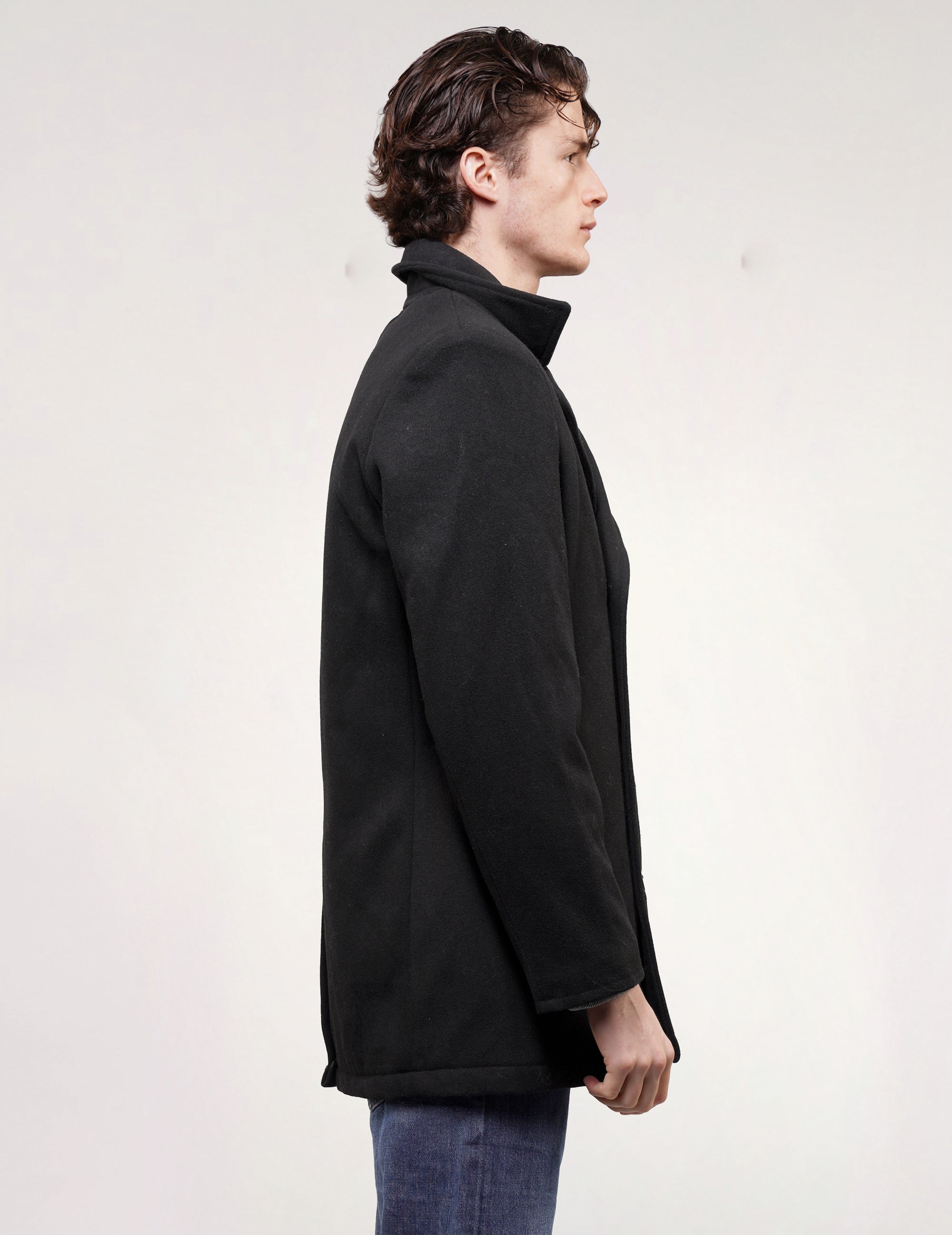 Side profile of model wearing a black wool-blend naval peacoat with long sleeves.