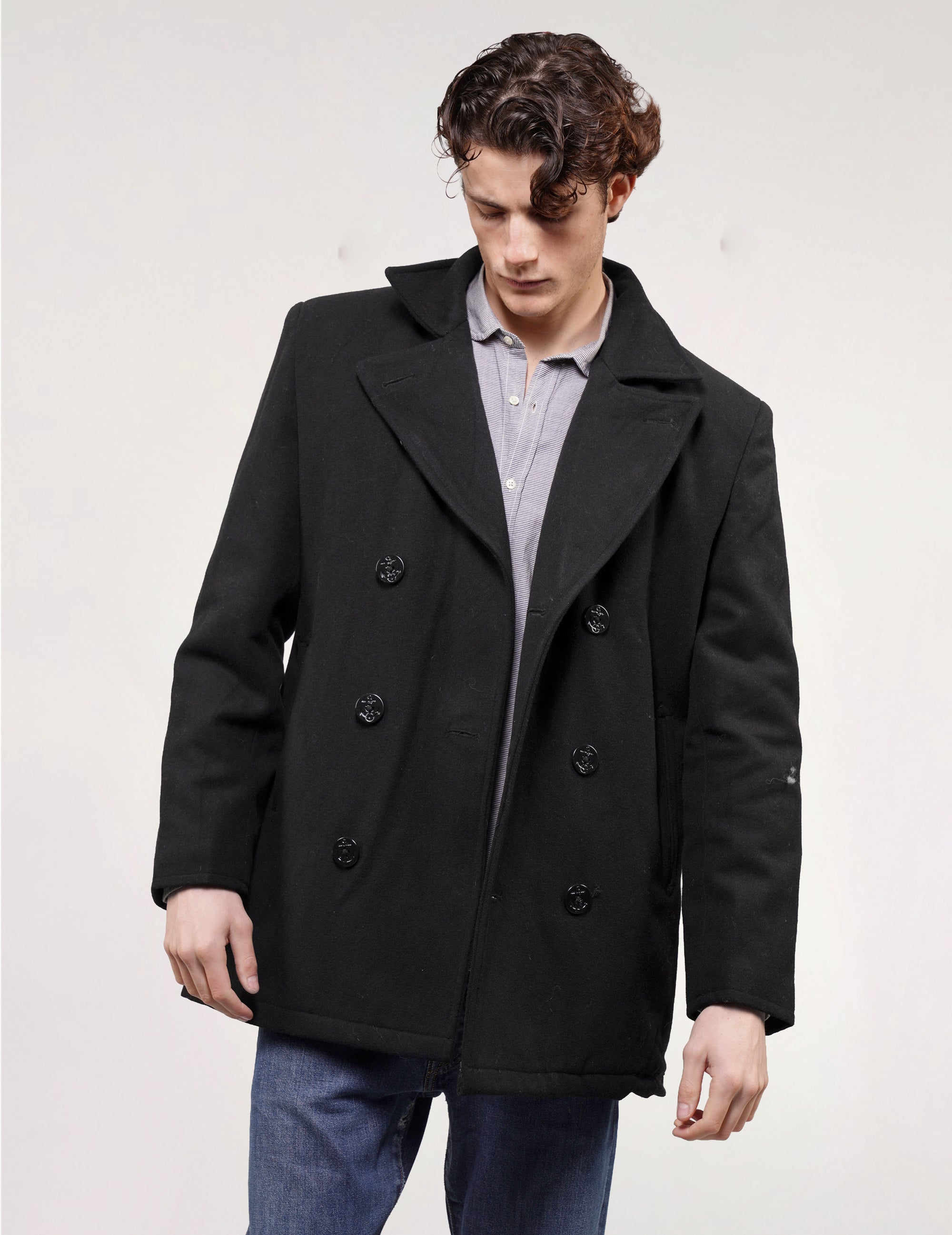 Model wearing a black double-breasted naval peacoat with anchor-style buttons, styled with jeans.